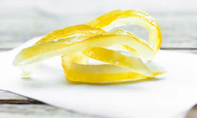 Gelbe Zitronenschalen-Streifen, die an das Selbermachen von Apfelpektin erinnern, liegen auf weißem Papier.