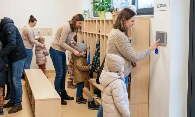 Rodzice odbierają dzieci z przedszkola. W szatni panuje ruch, dzieci ubierają się do wyjścia.