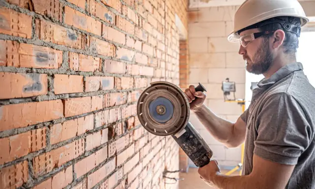 Obrero con casco y gafas protectoras listo para cortar pared con radial.