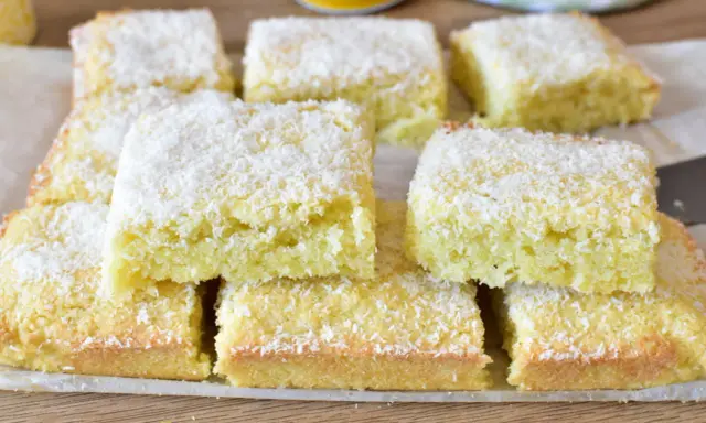 Fette di torta al cocco, soffici e dorate, cosparse di scaglie bianche. Un dolce profumato e invitante.