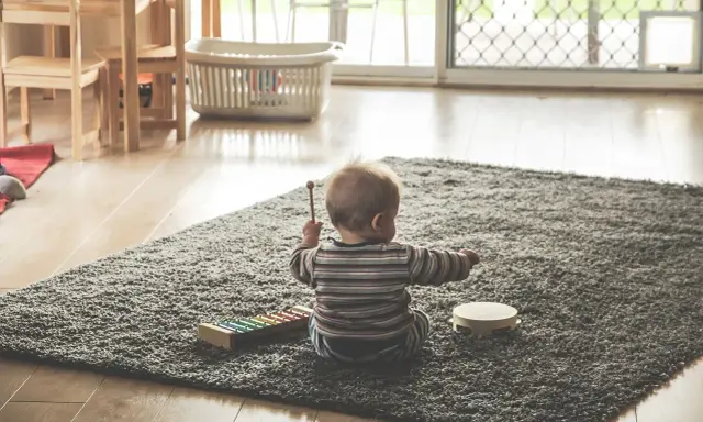 Liten bebis sitter på en matta och leker med en xylofon och en tamburin. En perfekt start på en checklista bebis för musikaliska äventyr.