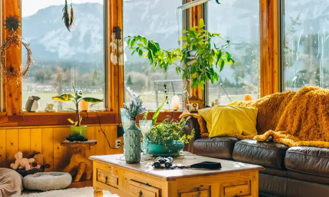 Un acogedor **salón estilo natural** con sofá de cuero, manta naranja, plantas y vistas a la montaña.