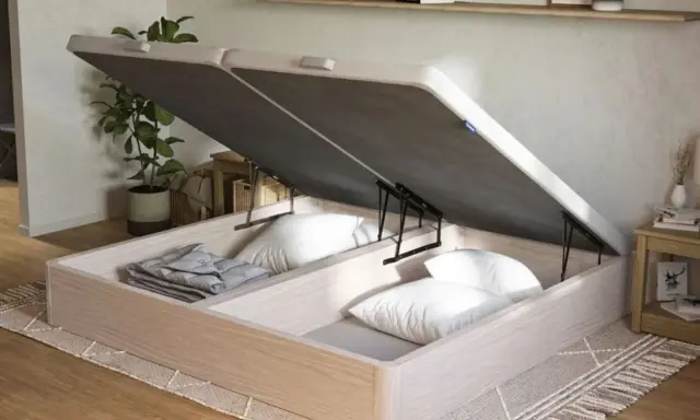 Un canapé de madera clara con la tapa abierta, revelando un gran espacio de almacenamiento para ropa de cama y almohadas.