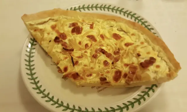 Part de quiche lorraine, une des spécialités lorraines, sur une assiette décorée de feuilles vertes.