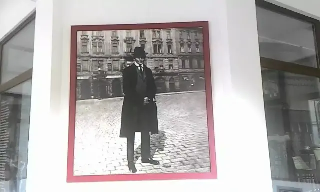 Ritratto di Franz Kafka, figura iconica che ci fa chiedere chi era Kafka, in piedi su un selciato con un edificio sullo sfondo.