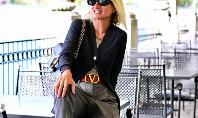 Donna con pantalone grigio elegante, abbinato a cardigan scuro e cintura con logo dorato. Un look chic per ogni occasione.