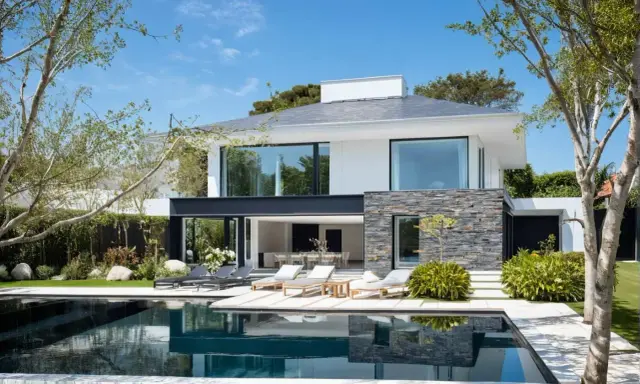 Une maison moderne simple avec piscine, terrasse et mobilier de jardin. Le soleil brille sur cette demeure épurée.