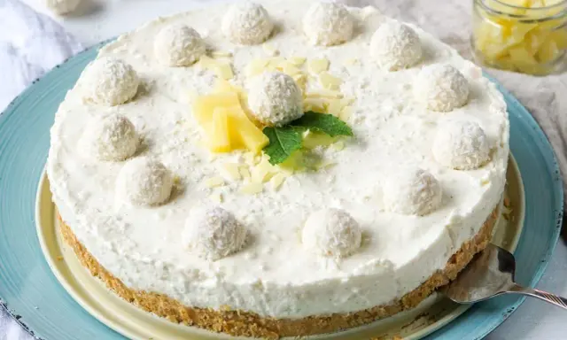 Eine köstliche Raffaello Torte ohne Backen, dekoriert mit Kokosbällchen, Ananas und Minze.