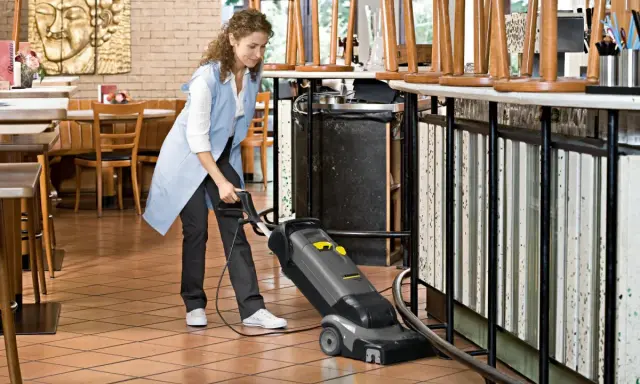 Kobieta sprząta podłogę w restauracji za pomocą odkurzacza. Dowiedz się, czym czyścić linoleum domowe sposoby.