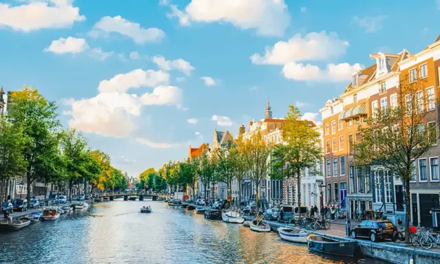 Widok na kanał w Amsterdamie, z łodziami, kamienicami i zielenią. Idealne miejsce, by poczuć, gdzie jest Amsterdam.