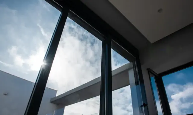 El sol brilla a través del vidrio guardian, iluminando un cielo azul con nubes blancas.