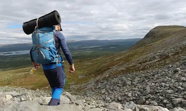 Vandrare med ryggsäck och liggunderlag på väg nerför en stenig fjällsida. En perfekt packlista vandring för äventyret.