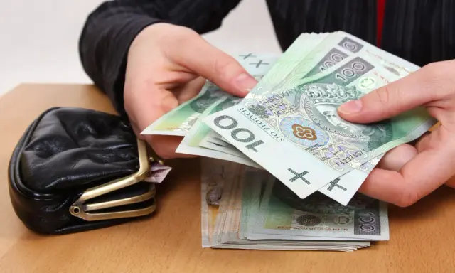 Dłonie liczą banknoty 100 zł obok portmonetki. Zastanawiasz się, ile wynosi trzynasta emerytura netto?