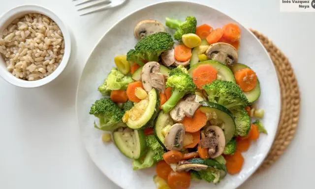 Un colorido salteado de verduras con brócoli, zanahoria, calabacín y champiñones, servido junto a un tazón de arroz integral.
