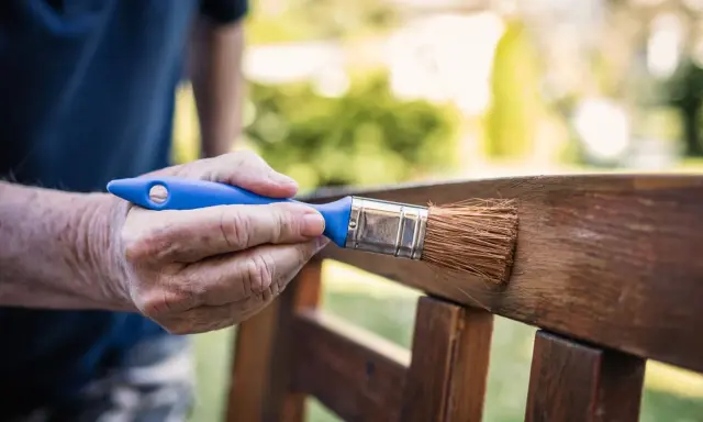 Mano aplicando barniz a un banco de jardín, creando un hermoso efecto madera.