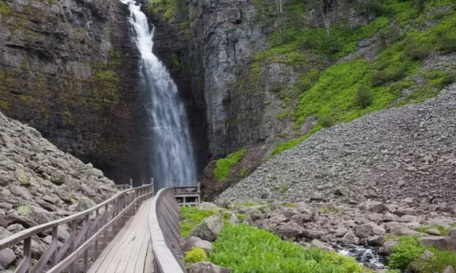 Vacker vattenfall i en ravin, med en träbro som leder besökare längs en av Sveriges många vandringsleder.