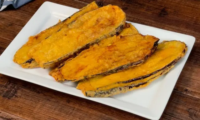 Fette di melanzane fritte, dorate e croccanti, servite su un piatto bianco. Un assaggio delle deliziose melanzane alla pullastiello.