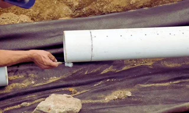 Main tenant applique un produit sur un tuyau blanc pour comment déboucher une canalisation enterrée.