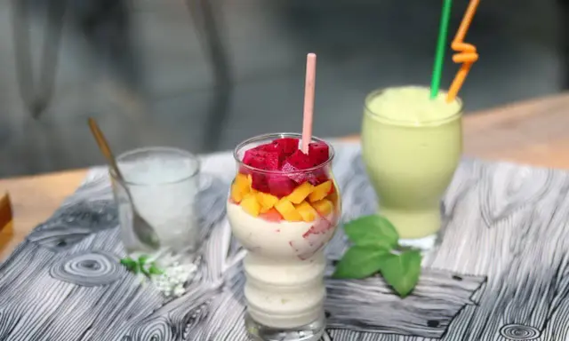 Pyszny koktajl białkowy z kawałkami smoczego owocu i mango. Obok zielony smoothie i szklanka z lodem.