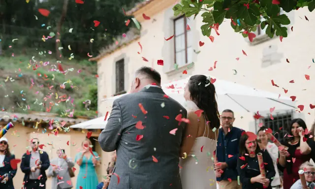 Novios bajo una lluvia de confeti en forma de corazón. Los invitados lanzan confeti, creando un ambiente festivo, perfecto para las canciones de boda.