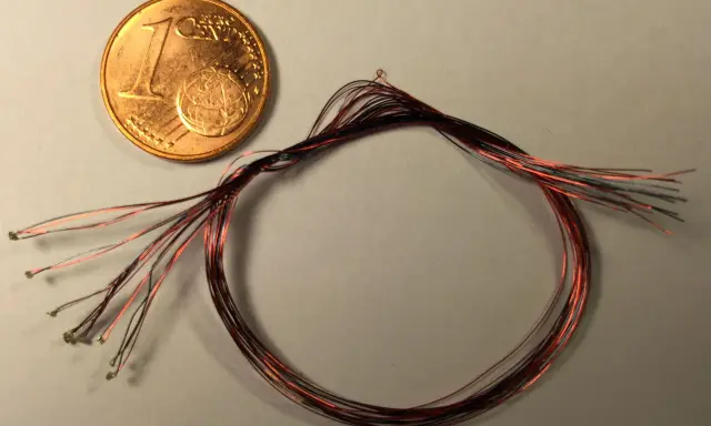 Ein-Cent-Münze neben einem Bündel dünner roter und schwarzer Kabel mit kleinen Lötpunkten.