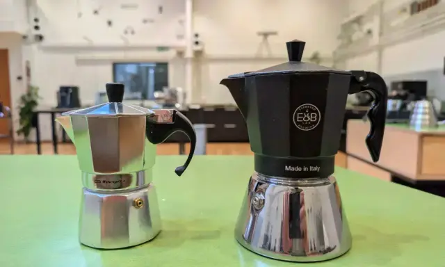 Zwei Espressokocher, ein silberner und ein schwarzer, stehen bereit für den perfekten Espresso auf dem Herd.