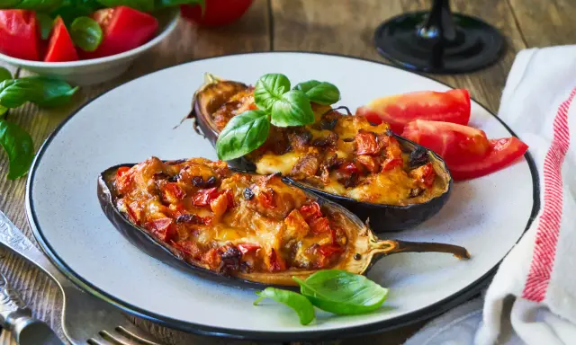 Melanzane ripiene senza carne, dorate e filanti, guarnite con basilico fresco e pomodoro. Un piatto vegetariano invitante.