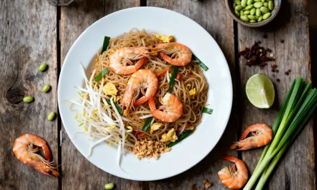 Délicieux Pad Thaï aux crevettes, une recette simple et savoureuse. Nouilles, pousses de soja, œuf, oignons verts et crevettes.