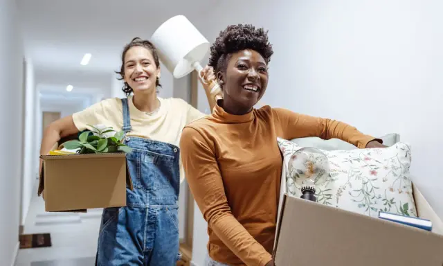 Deux amies souriantes déménagent, portant des cartons remplis d'objets. Une nouvelle aventure commence, peut-être grâce à un **bail solidaire**.