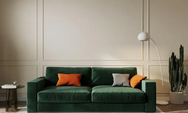 Elegancki salon w odcieniach butelkowej zieleni i beżu. Miękka sofa, nowoczesna lampa i kaktus tworzą przytulną atmosferę.