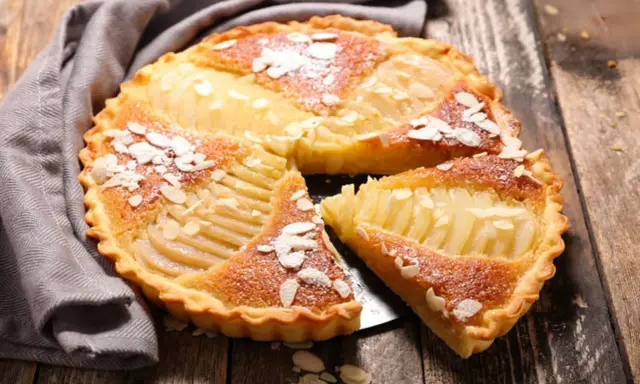 Une délicieuse tarte aux poires, garnie d'amandes effilées et saupoudrée de sucre glace, repose sur un plateau en bois.