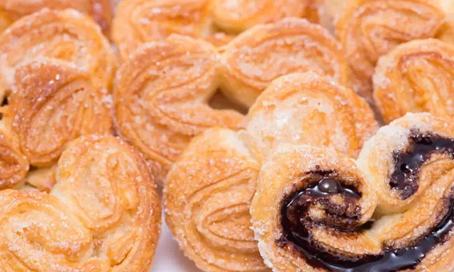 Deliciosas palmeritas de hojaldre espolvoreadas con azúcar. Algunas tienen un relleno de chocolate oscuro y brillante.