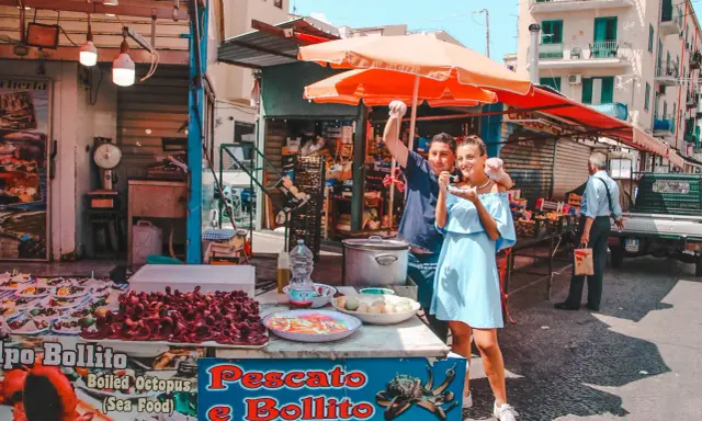 Coppia felice assaggia polpo fritto in un mercato di Palermo in un giorno di sole. Un assaggio autentico della Sicilia.
