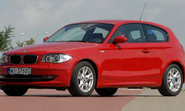 Czerwone BMW 116i z polskimi tablicami WI 3766G zaparkowane na czerwonym chodniku.