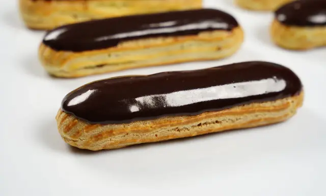 Plusieurs éclairs au chocolat brillants, avec un fondant pour éclair parfait, sont disposés sur fond blanc.