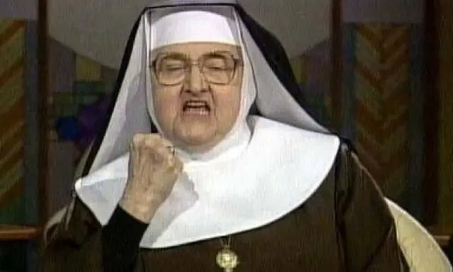 Zakonnica w okularach z zaciśniętą pięścią i otwartymi ustami.