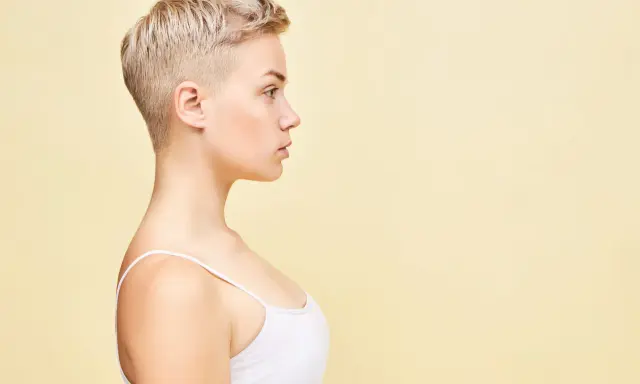 Perfil de una mujer joven con un moderno corte pixie rubio, luciendo un top blanco.