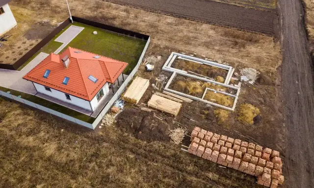 Działka rolno budowlana z gotowym domem i fundamentami pod kolejny. Materiały budowlane czekają na rozpoczęcie prac.