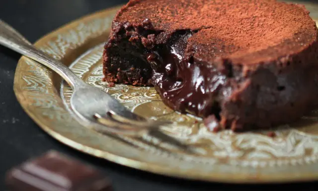 Fondant au chocolat cacao, cœur coulant, saupoudré de cacao, sur une assiette dorée avec une fourchette.