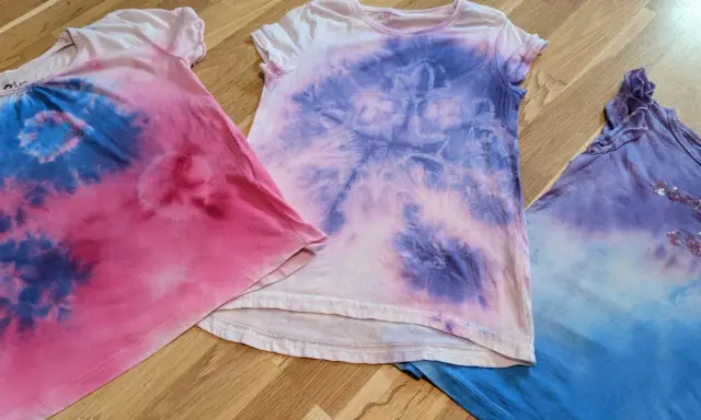 Batik mit Kindern: Drei bunte T-Shirts in Rosa, Lila und Blau, die nach einem kreativen Nachmittag aussehen.