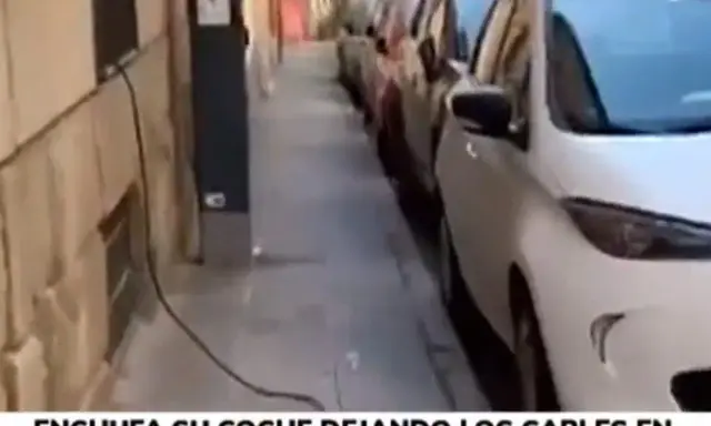 Un coche eléctrico se carga en la calle, con cables cruzando la acera. Una forma poco convencional de como cargar coche electrico en la calle.