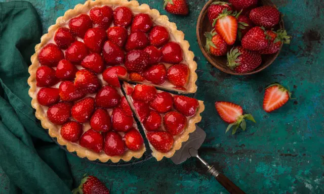 Une magnifique tarte aux fraises, garnie de fruits rouges brillants, est prête à être dégustée. Une part a été coupée, révélant la crème onctueuse.