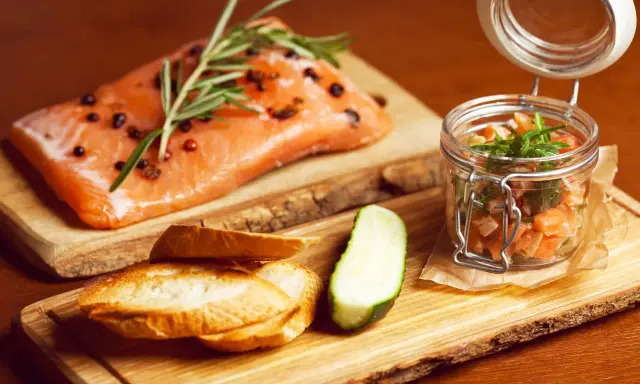 Świeży łosoś z rozmarynem i pieprzem, tartare w słoiczku, pieczywo i ogórek. Zdrowe łosoś kcal na drewnianej desce.