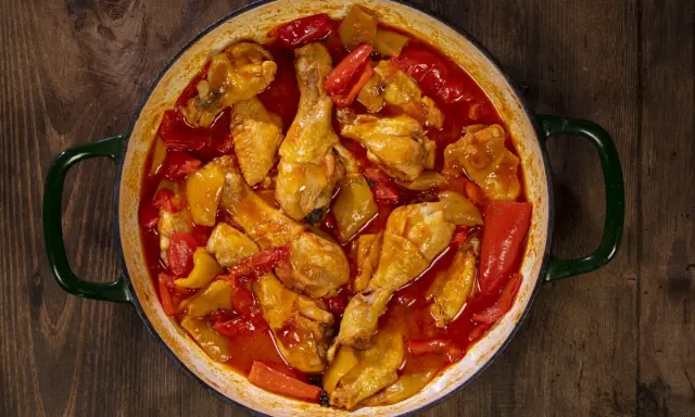 Un saporito pollo con peperoni in umido, cotto in una casseruola verde su un tavolo di legno scuro.