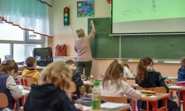 Nauczycielka dyplomowana pisze na tablicy, dzieci słuchają. Ciekawe, jakie nauczyciel dyplomowany zarobki ma w tej szkole.