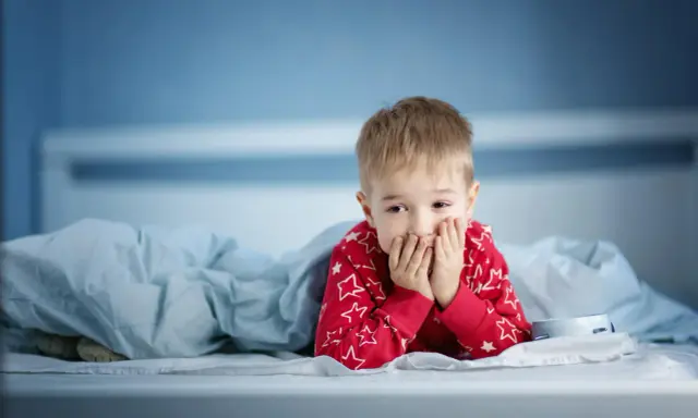 Zmartwiony chłopiec w piżamie z gwiazdkami leży w łóżku. Martwi się, że dziecko nie sika od 24 godzin.