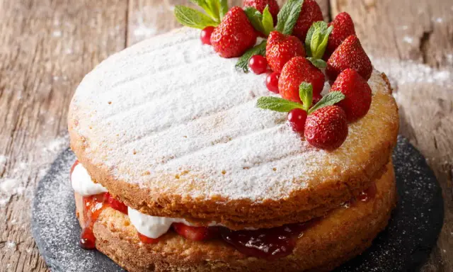 Gâteau génoise fraise, garni de crème, confiture et fruits rouges frais, saupoudré de sucre glace.