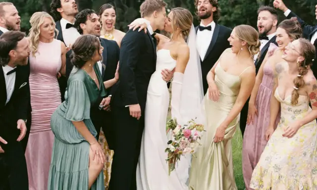A wedding party celebrates as the bride and groom kiss. The groomsmen attire is classic black tuxedos.