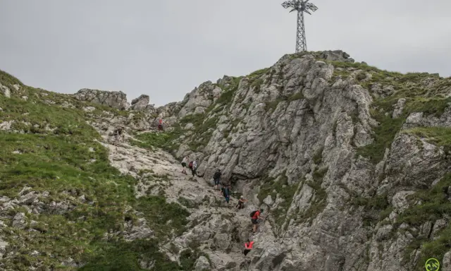 Grupa turystów wspina się po skalistym zboczu Giewontu w kierunku krzyża.