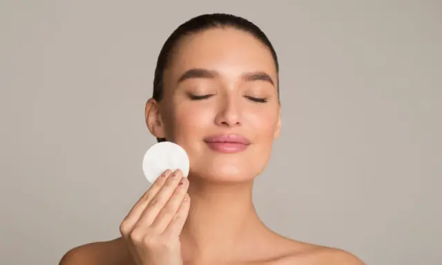 Donna con occhi chiusi applica un dischetto di cotone sul viso, parte della sua routine di skincare viso per una pelle radiosa.